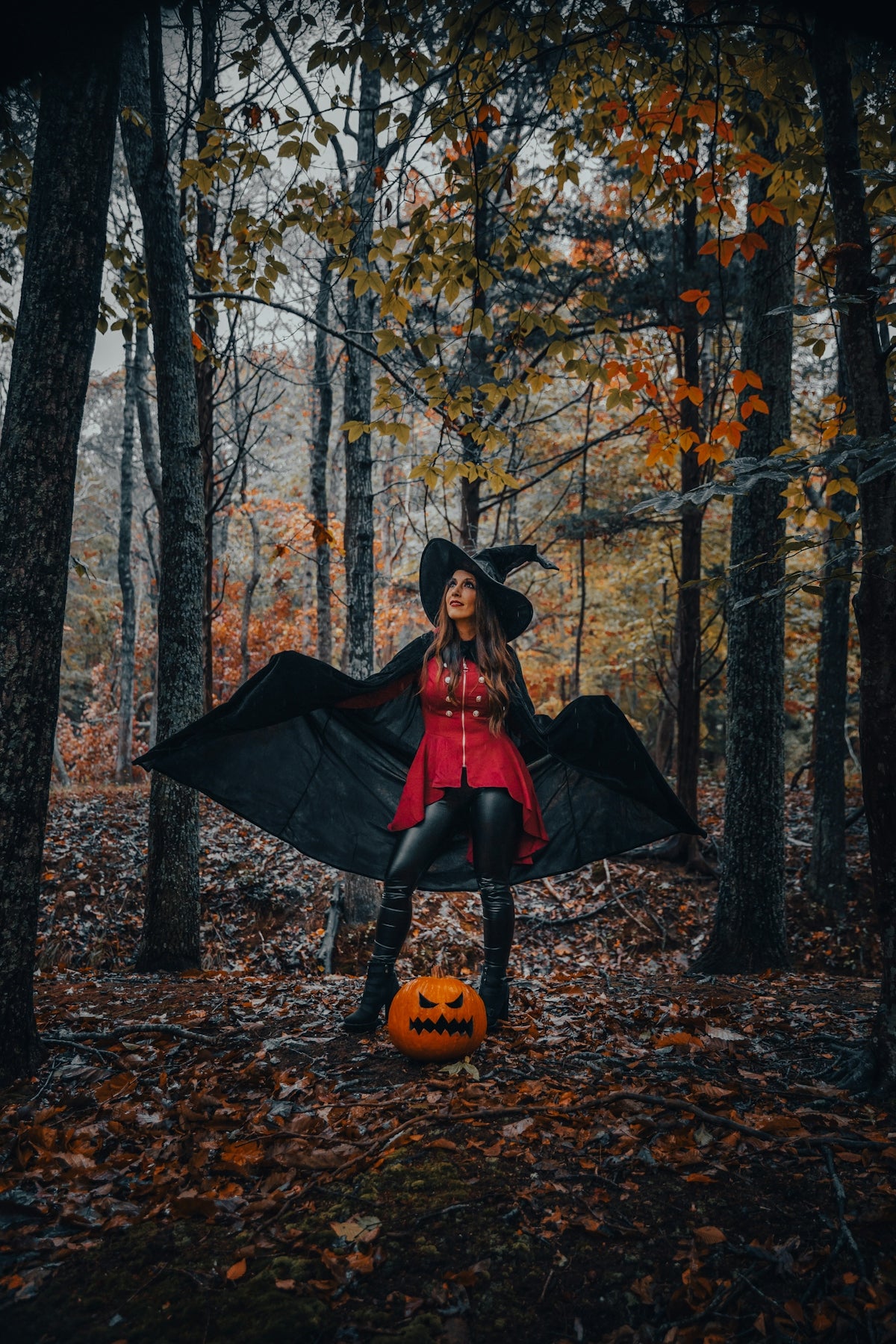 Witch in autumn forest with a carved halloween pumpkin